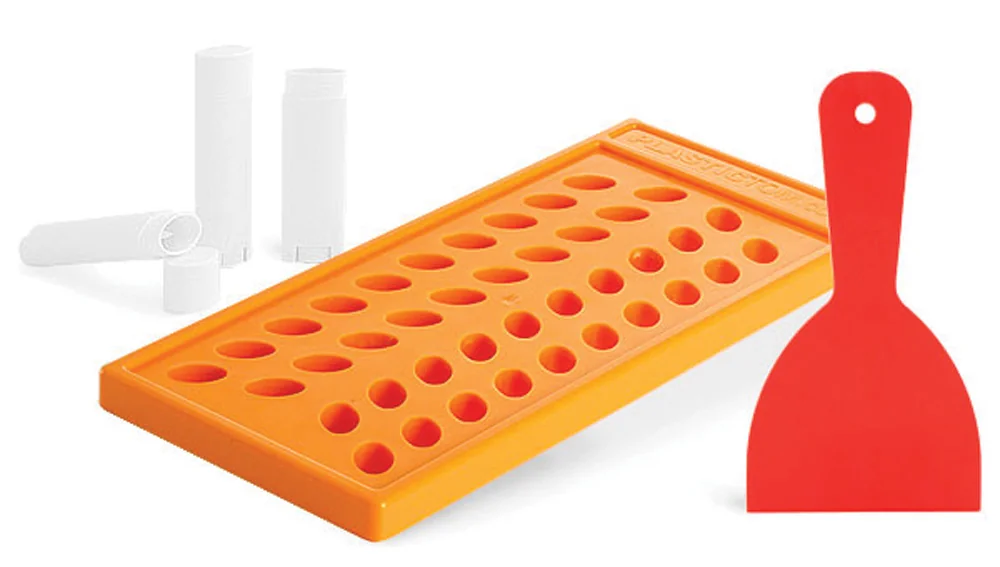 Orange silicone tray for filling lip balm tubes, with white tubes and a red scraper